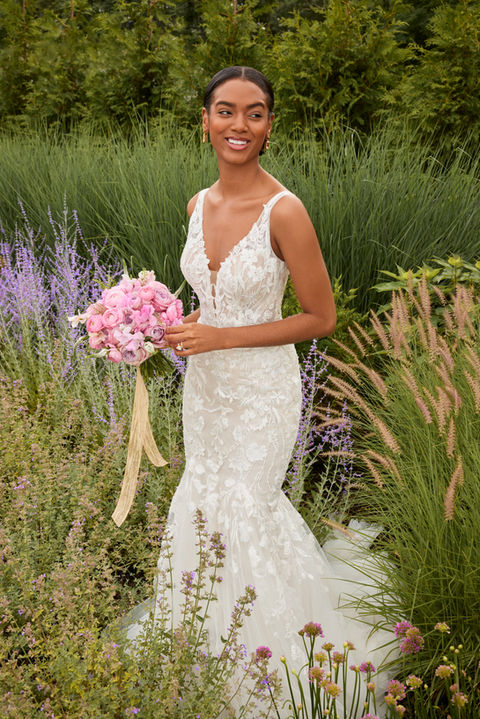 Our Sydney designer wedding dress is classic bridal beauty. The fitted gown has a plunging v-neckline that elongates the body and draws the eye down to the flared tulle skirt. Delicate floral embroidered lace appliqués have a feminine and romantic feel, accenting the sheer open back and climbing up the straps. Godet insets on the train add texture and drama.