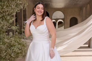 A study in sculptural romance,our Amelia ball gown features a stylized sweetheart neckline that curves into a delicately beaded, draped bodice, folded with precision. The dropped waist enhances the silhouette, flowing seamlessly into a dramatic duchess satin skirt that commands attention with its voluminous structure and fluid movement. A sweeping train completes the look, marrying timeless grandeur with modern edge.