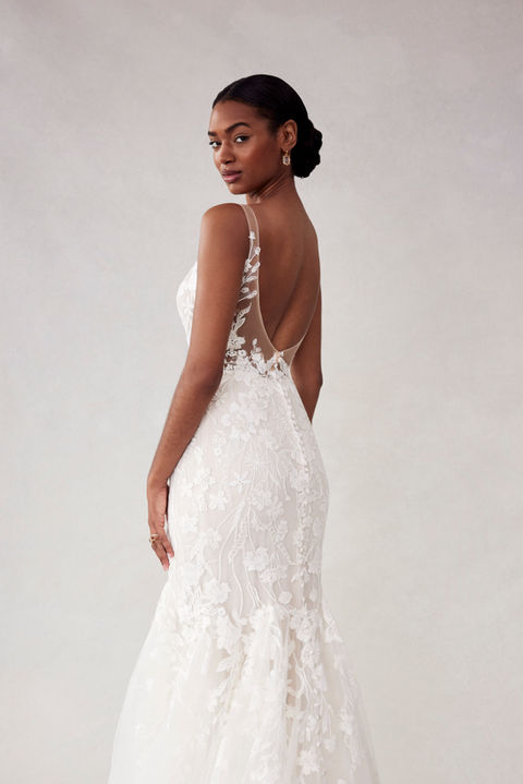 Our Sydney designer wedding dress is classic bridal beauty. The fitted gown has a plunging v-neckline that elongates the body and draws the eye down to the flared tulle skirt. Delicate floral embroidered lace appliqués have a feminine and romantic feel, accenting the sheer open back and climbing up the straps. Godet insets on the train add texture and drama.