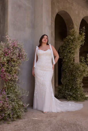 Our Junia wedding dress balances classic bridal and modern style. The fit and flare gown stuns with a modified sweetheart neckline and delicate tie shoulder straps. The corset back sculpts the bodice, while intricate floral appliqué cascades over the silhouette, bringing movement and texture. A sheer organza overskirt with hidden pockets adds volume and versatility for a transformative look. Shown in Ivory/Champagne. Organza Overskirt with Pockets sold separately as Style 11612. This gown is available without the overskirt as Style 3474D.