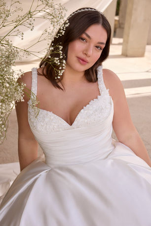 A study in sculptural romance,our Amelia ball gown features a stylized sweetheart neckline that curves into a delicately beaded, draped bodice, folded with precision. The dropped waist enhances the silhouette, flowing seamlessly into a dramatic duchess satin skirt that commands attention with its voluminous structure and fluid movement. A sweeping train completes the look, marrying timeless grandeur with modern edge.
