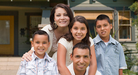 Smiling family of five posing in front of a house with a garden and yellow front door.