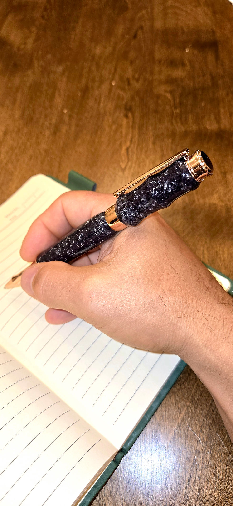 Gold roller ball pen wiht black starry night body in hand writing in an open jounal