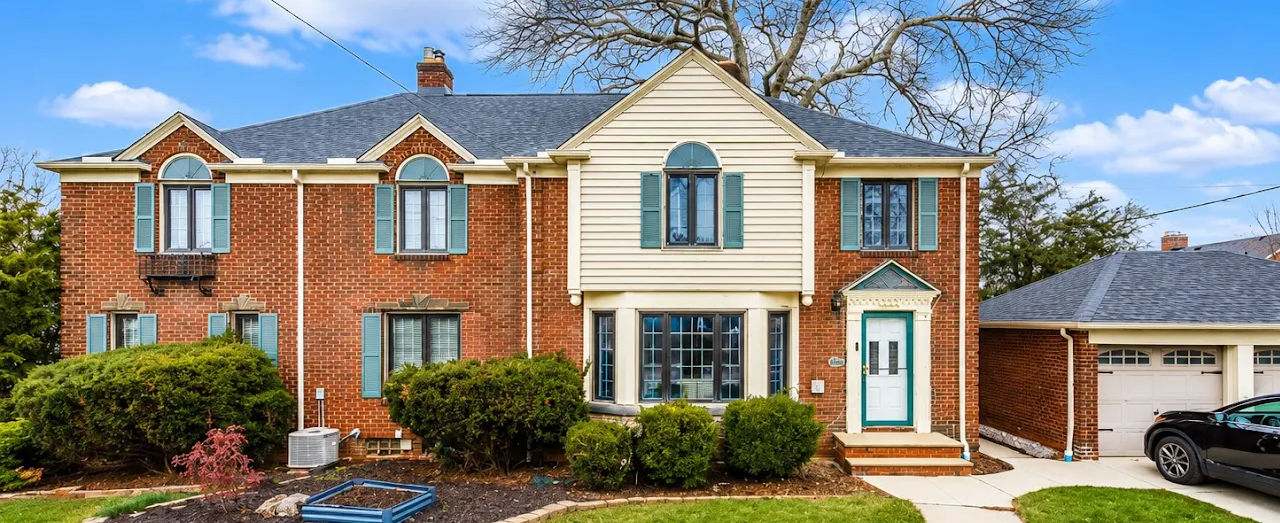 Two-story brick home with cream siding, landscaped front entrance, and mature trees.