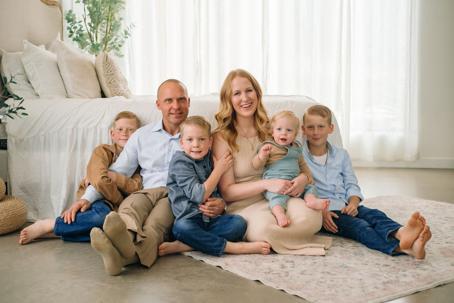 7. A family with four young children poses on a cozy bed in a bright studio during a McKinney family photography session serving Bonham and Collin County.