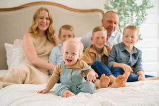 whole family snuggling on a bed with infant crawling around