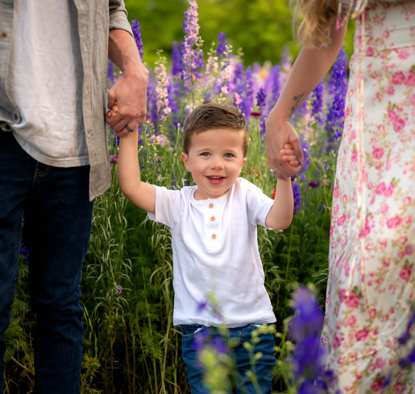 Little boy holding his parents’ hands while walking through the Richardson wildflowers — playful outdoor family photo.