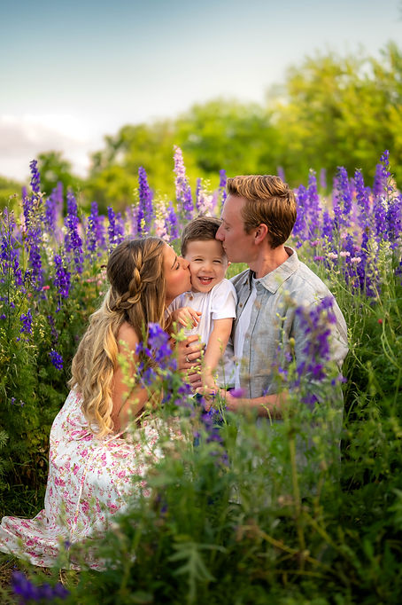 Parents kissing their laughing son surrounded by vibrant purple wildflowers in Richardson, TX — joyful and love-filled family portrait by Sweet Country Photography.