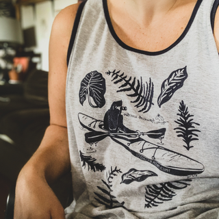 NRBC "Squatch Watchin" tank top design featuring Sasquatching in a kayak with a pair of binoculars. variety of plants surrounding him. Tank top is medium gray with blue ringer hem. Woman modeling tank.