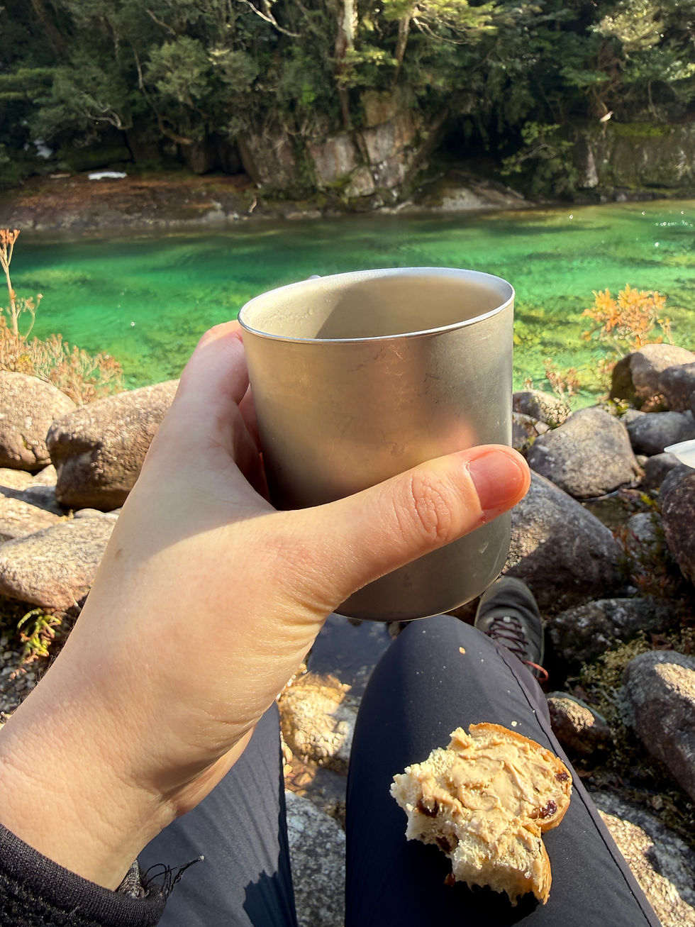 mel holding a coffee cup by the river with bread in their lap, from chicago doula mel haley's visit in 2026