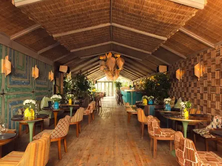 Long view of the Roofloor dining hall at Kabana Marrakech with vintage chairs and tropical wall art.