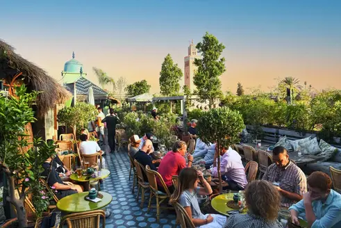 Terrasse animée sur le toit de Kabana, entourée d'un jardin suspendu avec vue sur la Koutoubia et une ambiance nocturne animée.