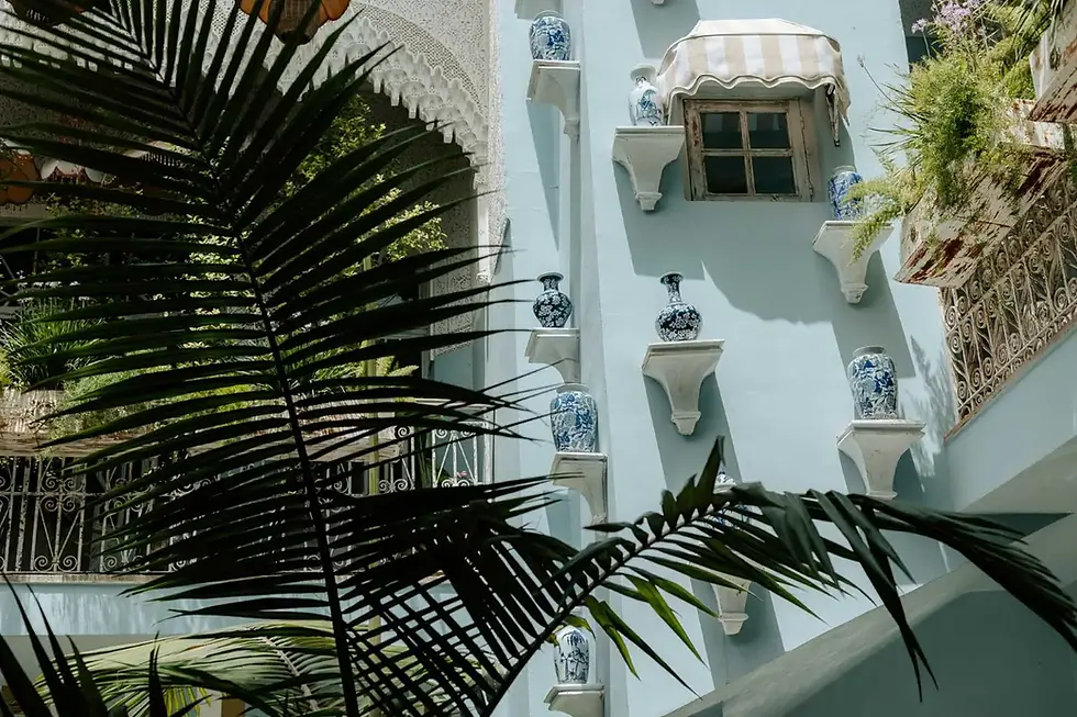 Terrasse intérieure de la cour du riad Villa Aaron à Marrakech avec des vases bleus traditionnels, des balustrades ornées et des ombres de palmiers