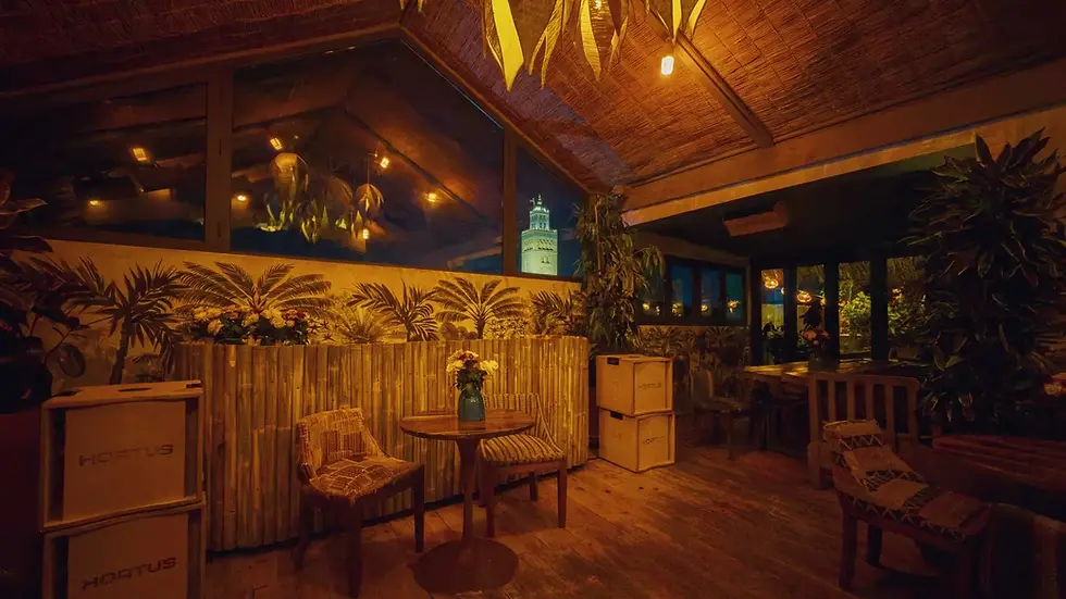 Kabana Roofloor interior at night, warm lighting, tropical décor and a framed view of the illuminated Koutoubia through the large window.