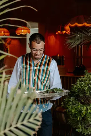 Serveur de la Villa Aaron en gilet traditionnel rayé servant des plats frais sur un plateau en argent dans un cadre de restaurant raffiné à Marrakech