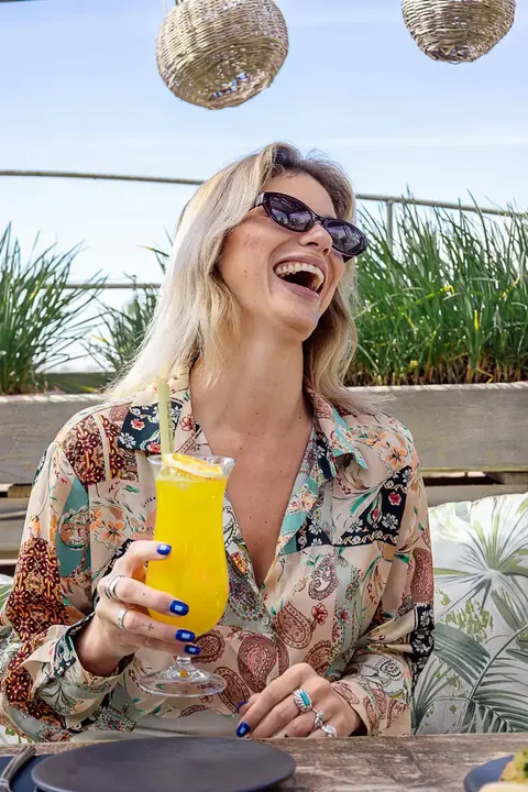 Young woman enjoying a refreshing orange juice cocktail under the sun at Kabana, the best rooftop in town in Marrakech.