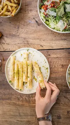Gros plan sur les cigares croustillants à la feta et à la menthe de Kabana à partager, servis avec des frites au parmesan et une salade fraîche sur une table en bois rustique.