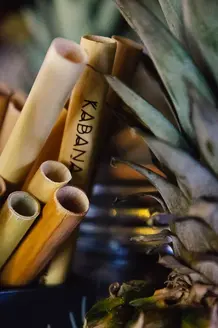 Des pailles en bambou Kabana nichées parmi des ananas aux reflets dorés, capturant une atmosphère tropicale au bar sur le toit.