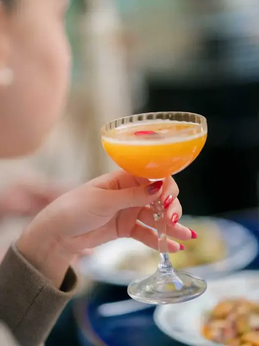 Hand holding a signature non-alcoholic cocktail with orange and rose petal at Villa Aaron in Marrakech