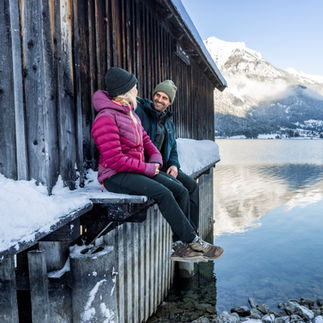 Winterliche Szene am Achensee mit verschneiter Landschaft, Bergen im Hintergrund und Gästen, die den Ausblick auf die Tiroler Bergwelt genießen