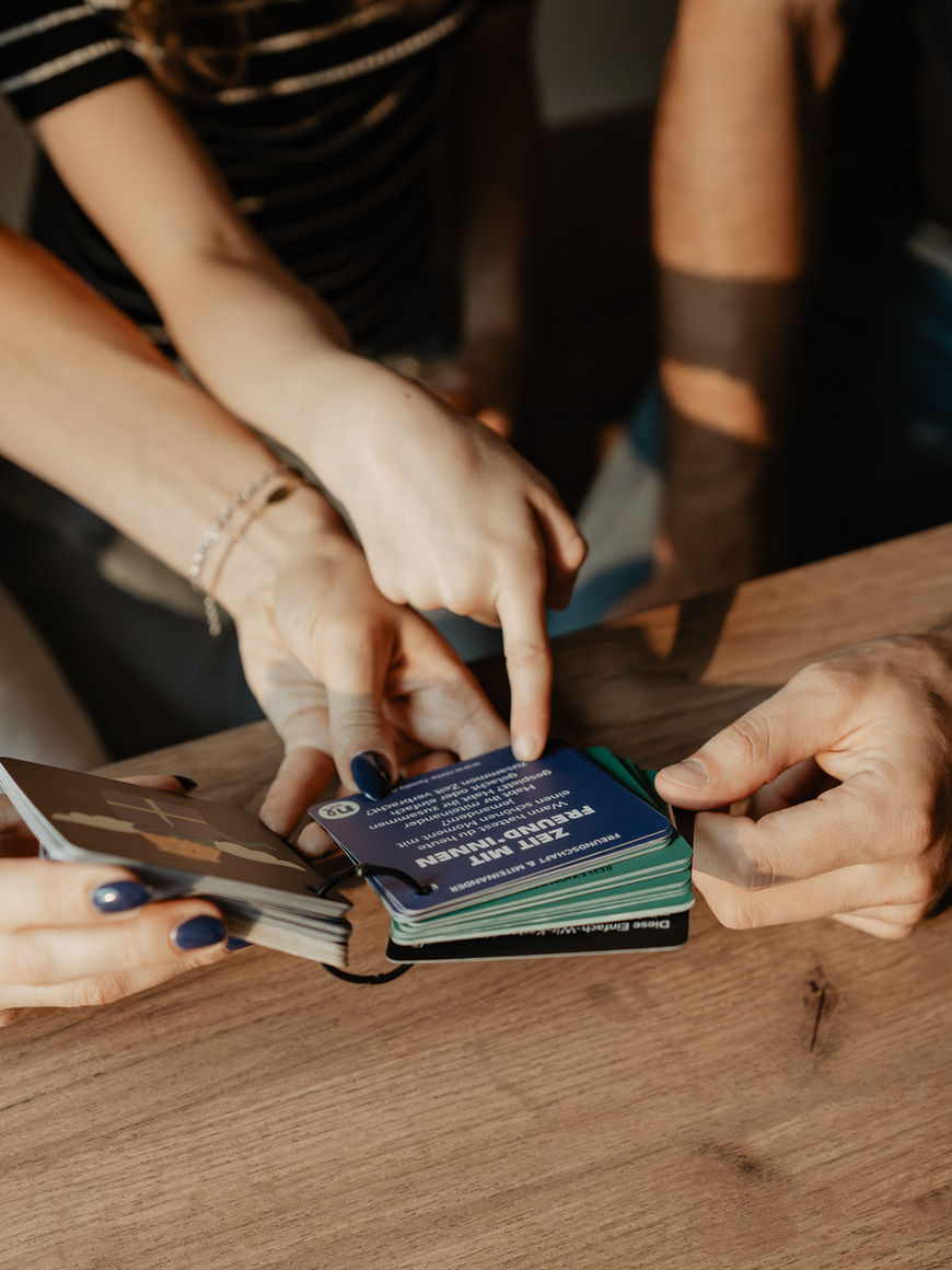 Hände greifen nach farbigen Karten, Einfach-Wir-Karten, die auf einem Holztisch liegen. niela-family