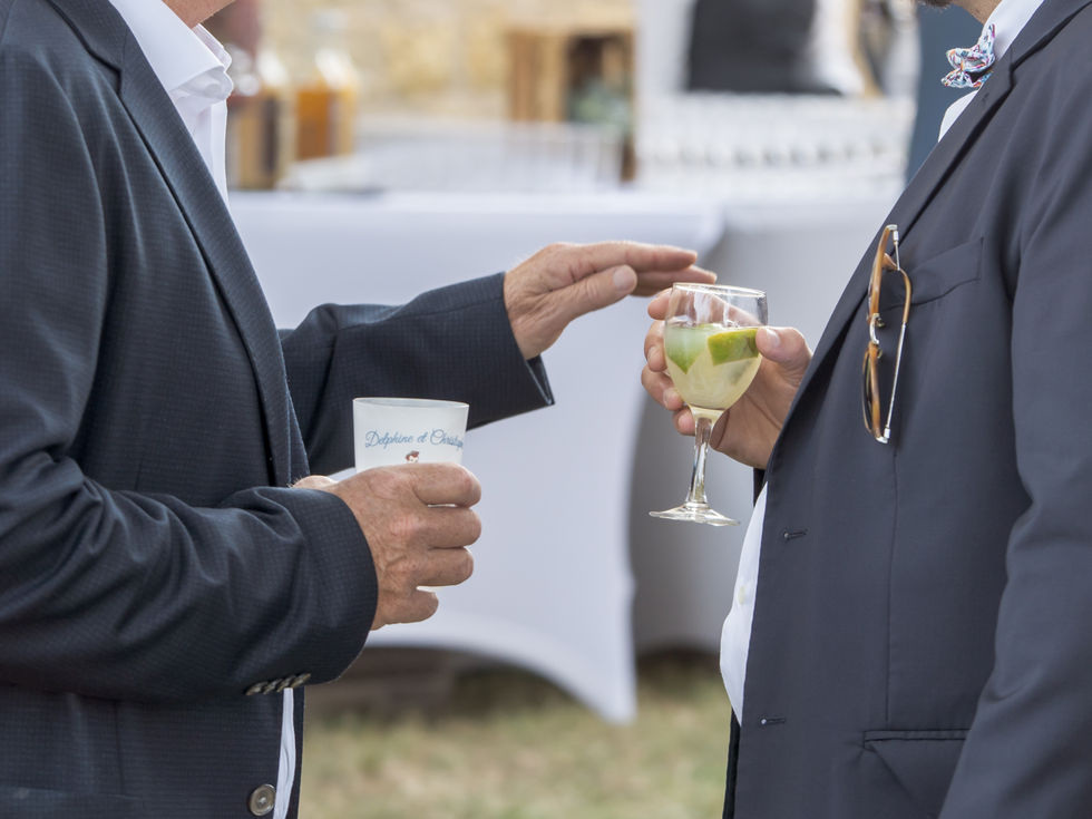 Deux hommes face à face dont on ne voit que les bustes, portent des verres au cocktail ; leurs mains semblent tenir conversation.