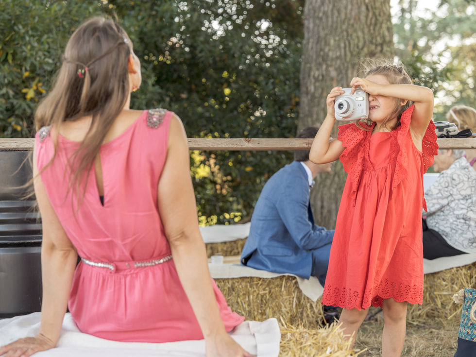 Une petite fille utilise un appareil photo instantané pour immortaliser une jeune femme qui prend la pose face à elle, dos au photographe.