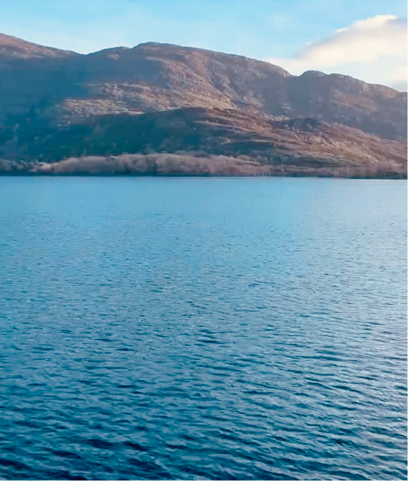 Calm blue lake with rippling water, surrounded by lush, sunlit hills under a clear blue sky. Peaceful and serene atmosphere.
