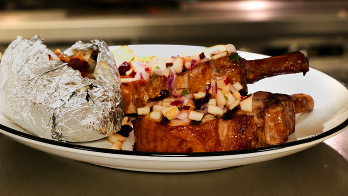 Char-grilled twin bone-in smoked pork chops with apple chutney and baked potato at Cappelletti’s