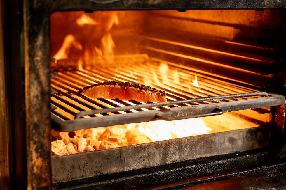 Salmon fillet grilling over open flames in a dark oven, glowing orange and smoky.
