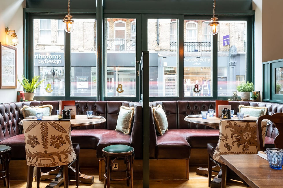 Cozy empty cafe with leather booths, patterned chairs and blue glasses by large windows; storefront signs visible outside.