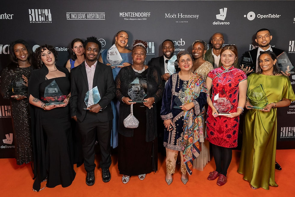 Diverse group posing on an orange carpet at the BIH Spotlight Awards, smiling and holding glass trophies before a logo wall.