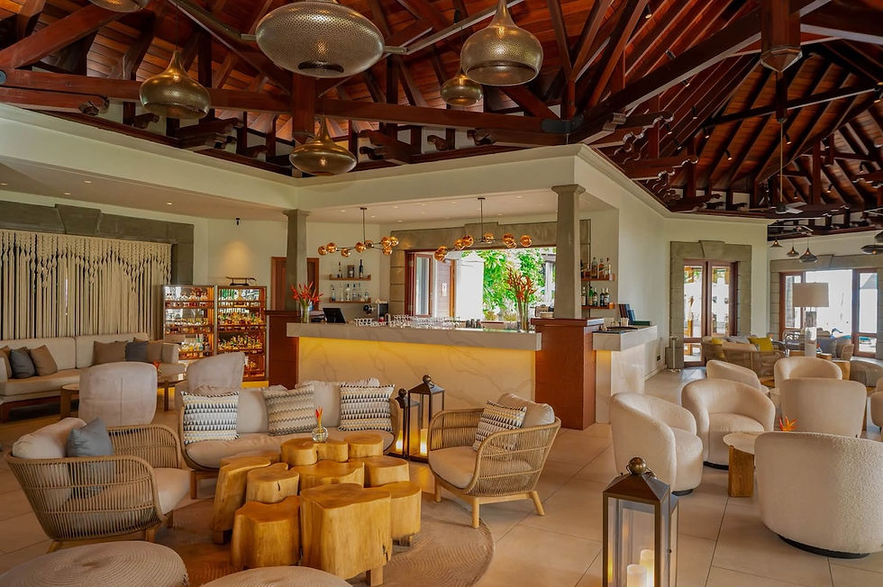Stylish tropical resort lounge with wicker chairs, wooden tables, and a lit bar beneath a high timber ceiling.