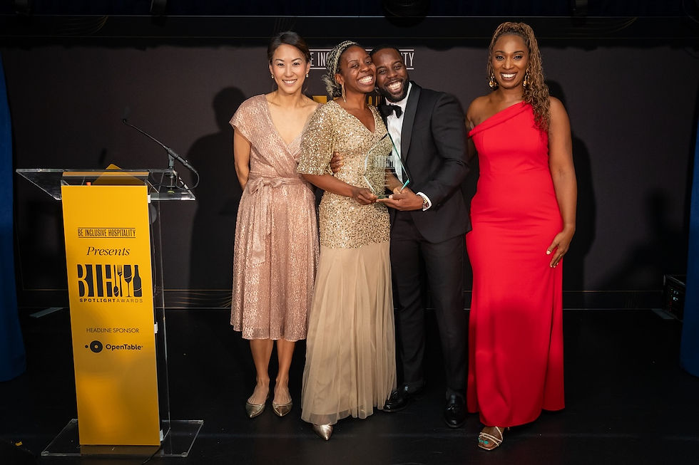 Four smiling award winners pose with a glass trophy on stage beside a podium for the BE Inclusive Hospitality BHI Spotlight Awards.