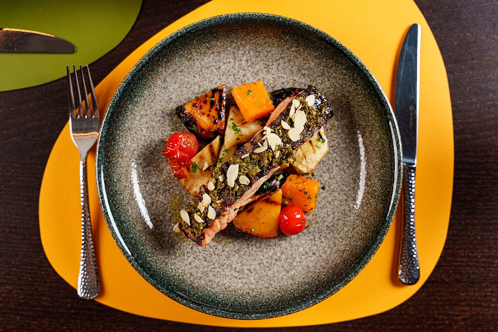 Gourmet fish and roasted vegetables on a gray plate with fork and knife on a bright yellow placemat.