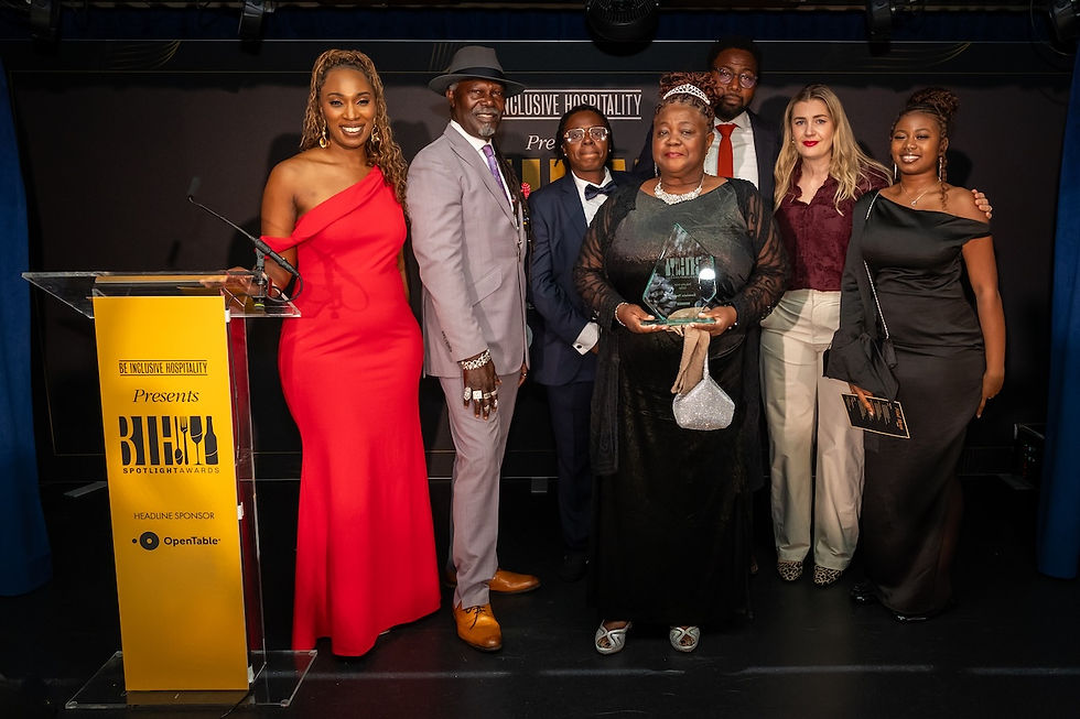 Group poses onstage at an Inclusive Hospitality Spotlight Awards, with one woman holding a glass trophy beside a yellow podium.