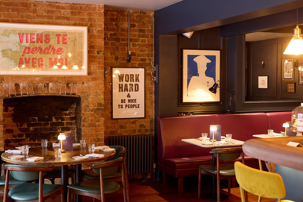 Cozy restaurant with brick walls, round tables, and red booths. Notable artwork includes "WORK HARD & BE NICE TO PEOPLE" poster. Warm lighting.