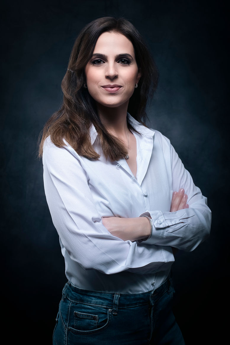 Sharon Gabay, woman with crossed arms in white shirt, jeans and background.
