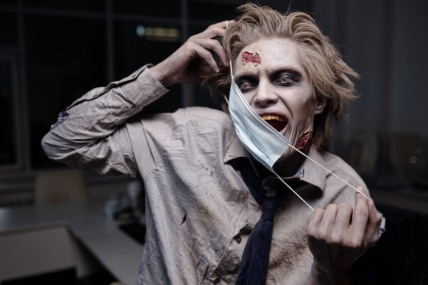 Scary zombie businessman holding surgical mask by his face