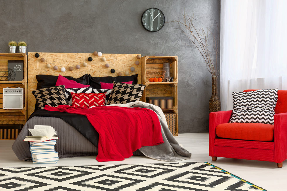 Bedroom with black and white houndstooth and geometric print pillows, a red blanket layered over gray bedding, and a black and white diamond patterned rug
