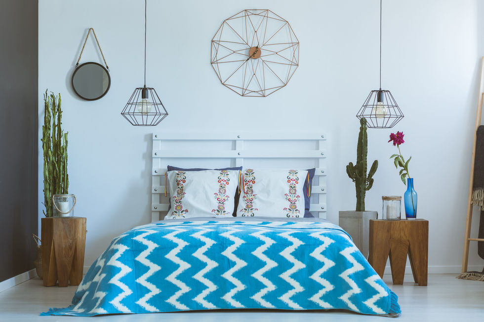 Bedroom with geometric wire pendant lamps, a white tufted headboard, a blue and white chevron patterned duvet, and potted cacti