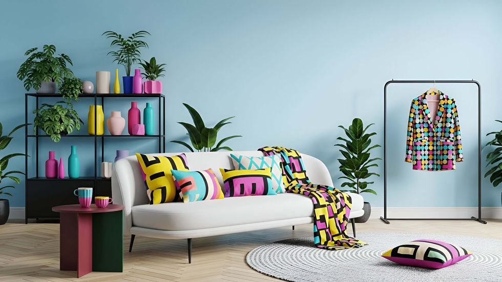 Pale blue living room with a white sofa styled with bold geometric color-block pillows and throw, a patterned blazer on a clothing rack, and a shelf of colorful vases