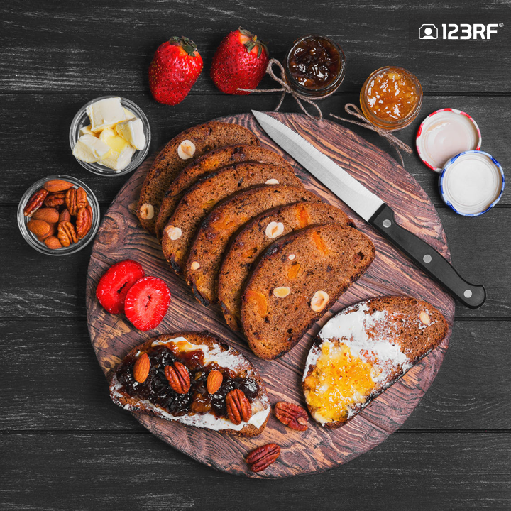 Stock Photo - Sweet dessert sandwiches crostini with lemon jam, plums jam, nuts pecans, hazelnuts, almonds, strawberries, rye bread with prunes and dried apricots for sandwiches, butter, cutting board on black wooden background