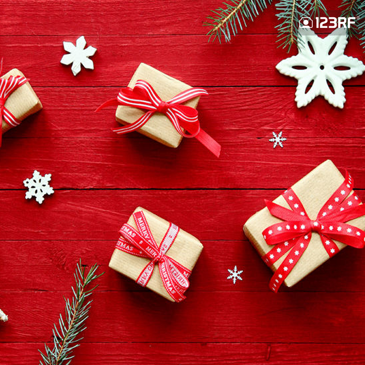 Stock Photo - Colorful red Christmas background with fresh pine branches, stars, snowflakes and decorative gifts tied with ribbon and bows scattered on a festive red background, overhead view