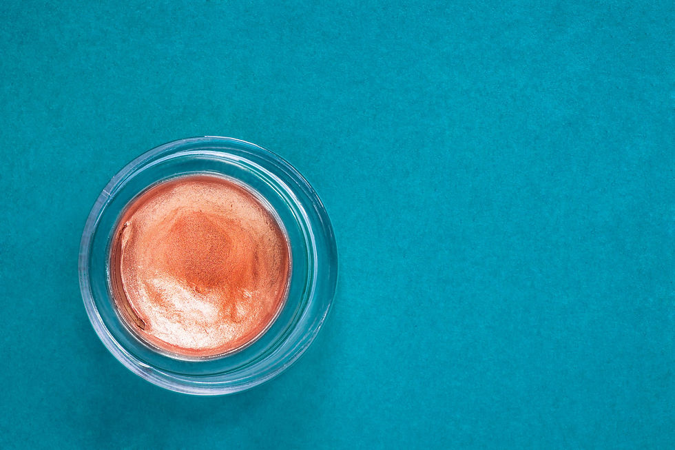 Shimmering rose-gold cream eyeshadow in a small glass jar on a teal background