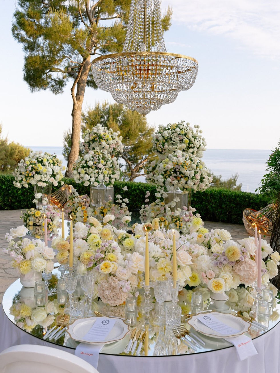 Elegant table setting with flowers and chandelier, overlooking the ocean background.
