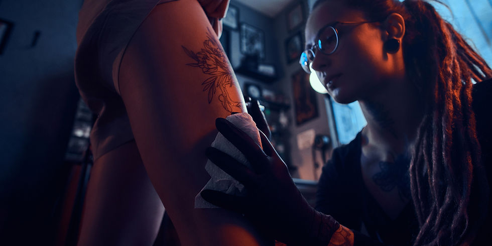 Tattoo artist with dreadlocks applying a new tattoo on a leg