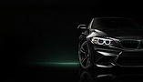 Close-up of a black BMW M2 front with glowing headlights