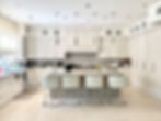 Elegant white kitchen with island, seating, and overhead lights; Legourmet Kitchen