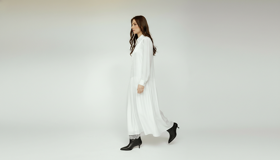 Woman walking in a long white pleated dress and black boots.